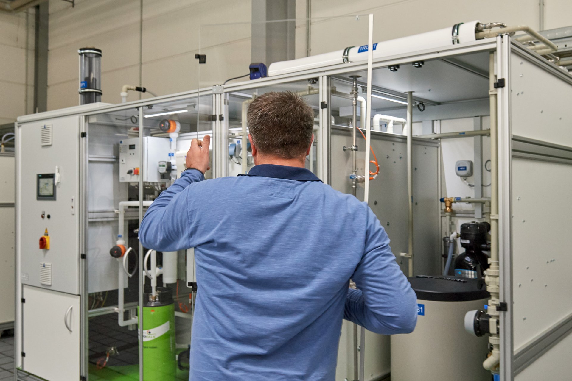 Mitarbeiter mit Glasscheibe in der Hand vor Wasseraufbereitungsanlage