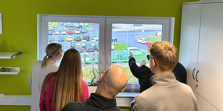 Mitarbeiter schauen einem Fenster auf den Firmenparkplatz